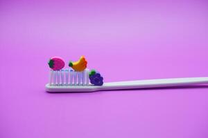 white toothbrush with fruit toys on it. White toothbrush isolated on purple background photo