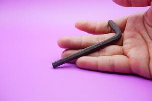 hand holding an L key. Allen key isolated on purple background photo