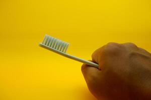 hand holding a white toothbrush. White toothbrush isolated on yellow background. photo