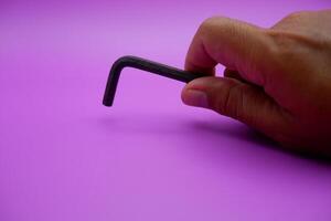 hand holding an L key. Allen key isolated on purple background photo