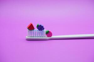 white toothbrush with fruit toys on it. White toothbrush isolated on purple background photo