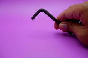 hand holding an L key. Allen key isolated on purple background photo
