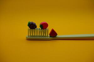 white toothbrush with fruit toys on it. White toothbrush isolated on dark yellow background photo