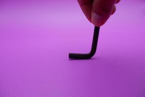 hand holding an L key. Allen key isolated on purple background photo