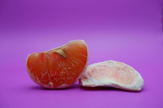 2 grapefruit isolated on purple background. 2 pieces of grapefruit that have been peeled until the grain of the orange is visible photo