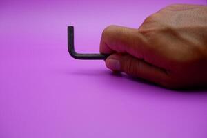 hand holding an L key. Allen key isolated on purple background photo