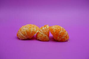 oranges that have been peeled and divided into several parts. orange isolated on purple background photo