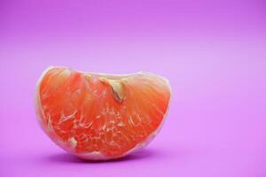 a slice of grapefruit isolated on a purple background. grapefruit that has been peeled until the grain of the orange is visible photo