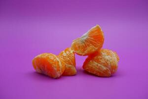 oranges that have been peeled and divided into several parts. orange isolated on purple background photo