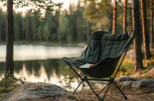 Black Folding Camp Chair Near Lake With Book in the Forest photo