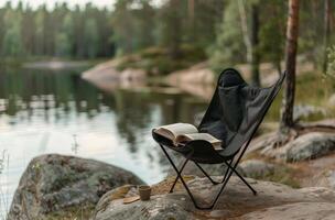 Black Folding Camp Chair Near Lake With Book in the Forest photo