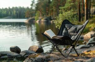 Black Folding Camp Chair Near Lake With Book in the Forest photo