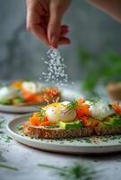 Hand Sprinkling Salt on Poached Egg Avocado Toast With Smoked Salmon and Dill photo