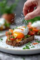 Hand Sprinkling Salt on Poached Egg Avocado Toast With Smoked Salmon and Dill photo
