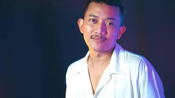Man with curly hair and mustache posing under colorful lights video