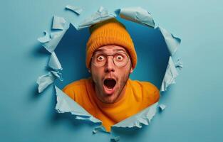 Shocked Man Peering Through Ripped Orange Paper on Blue Background photo