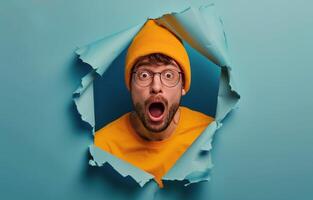 Shocked Man Peering Through Ripped Orange Paper on Blue Background photo