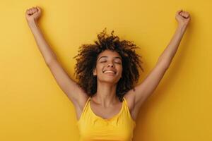 Woman With Curly Hair Smiles With Arms Raised In Front Of Yellow Background photo