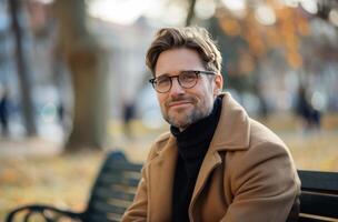 Smiling Man In Brown Coat Sitting On A Bench On An Autumn Day photo