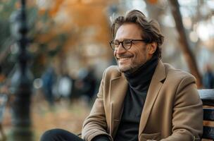 Smiling Man In Brown Coat Sitting On A Bench On An Autumn Day photo