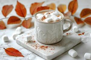 White Mug of Hot Chocolate With Marshmallows and Fall Leaves on a Marble Surface photo