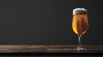 A single glass of beer with a thick head sits on a wooden tabletop photo