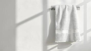 White towel on chrome rack against white wall with sunlight shadows photo