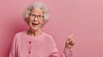 Happy elderly woman in a pink sweater pointing left against a bright pink backdrop photo