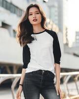 A woman wears a white and black raglan shirt with a blank front, posing casually against a city backdrop photo