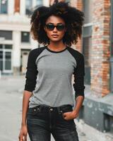 A stylish woman in a gray raglan shirt stands confidently against a brick wall photo