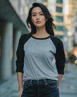 A woman wearing a grey raglan shirt with black sleeves stands in a city setting photo