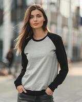 A woman poses with her hands in her pockets, wearing a blank gray and black raglan shirt photo