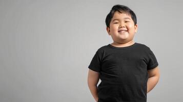 A happy Asian boy in a plain black t-shirt stands against a grey backdrop photo