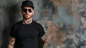 A man with tattoos and a rebel attitude stands confidently in front of a distressed wall, wearing a black t-shirt and a cap photo