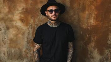 A man in a black t-shirt, sporting tattoos and a rebellious look, stands against a textured wall photo