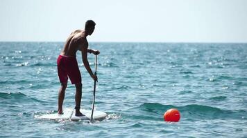 Man Sup Sea. Strong athletic man learns to paddle sup standing on board in open sea ocean on sunny day. Summer holiday vacation and travel concept. Aerial view. Slow motion video