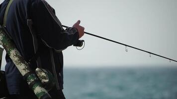 Man hobby fishing on sea tightens a fishing line reel of fish summer. Calm surface sea. Close-up of a fisherman hands twist reel with fishing line on a rod. Fishing in the sea outdoors. Slow motion. video