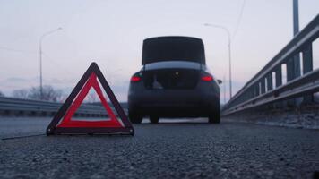 Broken-down car is parked on the side of the road. Its emergency lights are flashing and a bright red warning sign is visible in the foreground. video