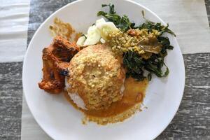 a portion of nasi Padang served on a table. which consists of grilled chicken, cucumber, cassava leaves and rice covered in a very delicious sauce. typical food from Sumatra, Indonesia photo