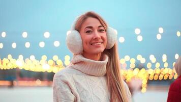 Smiling woman in earmuffs outside ice rink during Christmas video