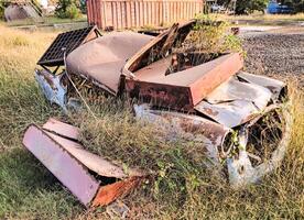 Broken abandoned car covered with rust in dry grassy field near tall trees against in Indonesian countryside photo