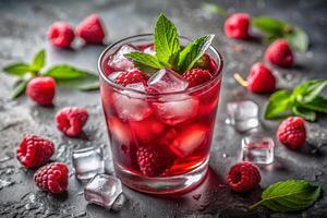 Close-up image of a refreshing red drink with ice and raspberries, garnished with a green leaf, with scattered ice pieces on a gray background photo
