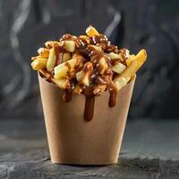 Poutine, Canadian fast food dish of french fries topped with cheese curds and gravy, in a paper cone container photo