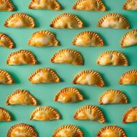 Pattern of golden brown empanadas on a turquoise background. Argentinian, Latin American food, flat lay, food photography, pattern design. photo