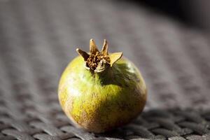 An unripe green pomegranate on a wicker brown table in the sunlight. An autumn fruit. Healthy food. Horizontal photo