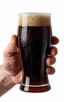 Close up of a man's hand holding a glass with dark beer isolated on a white background photo