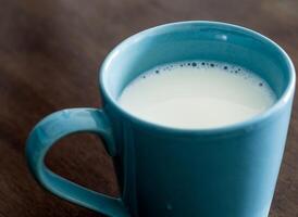Milk in a blue cup on the wooden and top glass table photo