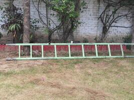 a green fence with a red border and a white brick wall with a tree in the background. photo