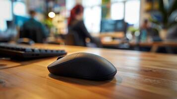 Wireless mouse on desk in busy office. Black wireless computer mouse on wooden desk, with blurred background of people working in a modern office. photo