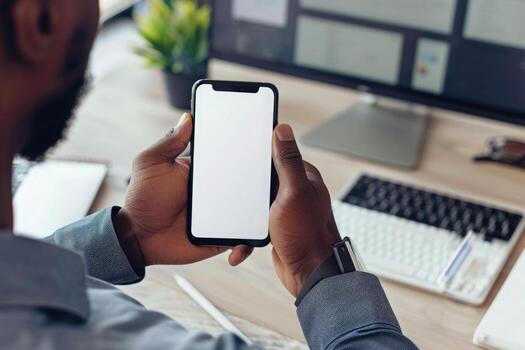 Mockup of a man's hands holding smart phone with blank white screen while sitting at the wooden table in modern office photo